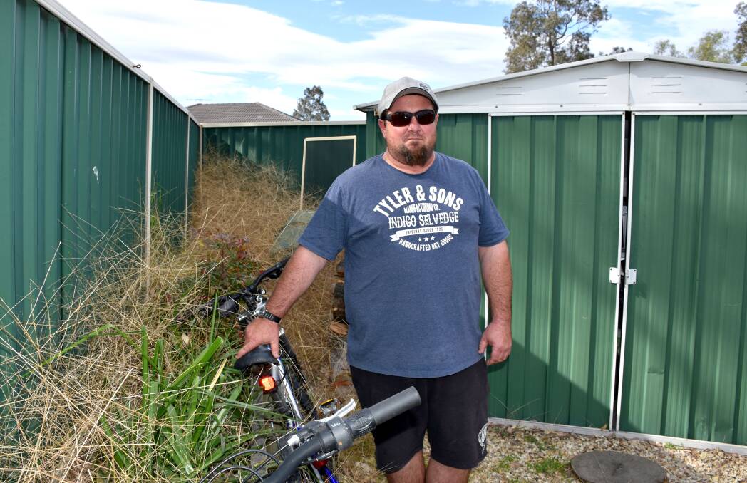 Singleton Heights resident Jamie Buckett in his backyard filled with spinifex grass blown in from the neighbouring vacant block of land.