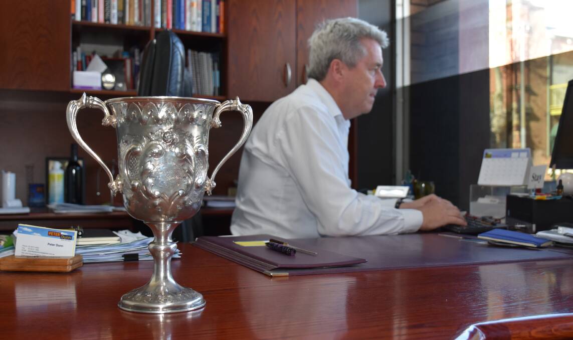 THE CUP RETURNS HOME: Real estate agent Peter Dunn pictured hard at work alongside his new possession.